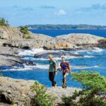 Two men are walking on cliffs by the sea on a sunny summer day.