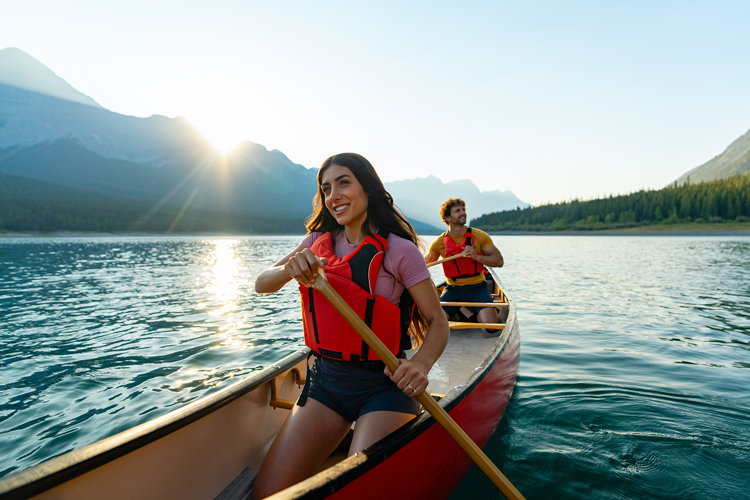 Two people take in the 360 degree mountain
views as the canoe across a lake together close to
sunset.